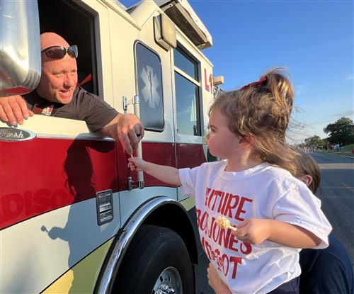 girl getting candy handed to her by a fireman